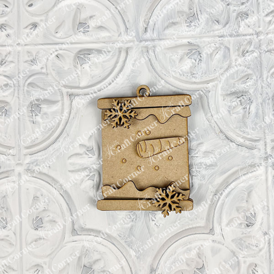 Janet's Craft Corner Snowman Ornaments DIY holiday craft kit (set of 1) features a wooden scroll-shaped ornament with snowflakes and a snowy log design, ideal for festive décor, shown on a white textured background with ornate patterns.
