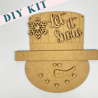 Introducing the DIY Snowman Door Hanger kit from Janet's Craft Corner for your home décor. This charming set includes the "Let it Snow" text, a delightful snowflake design, a round base for the snowman's face, pre-drilled holes for eyes and buttons, and a carrot-shaped nose piece to bring your creation to life.