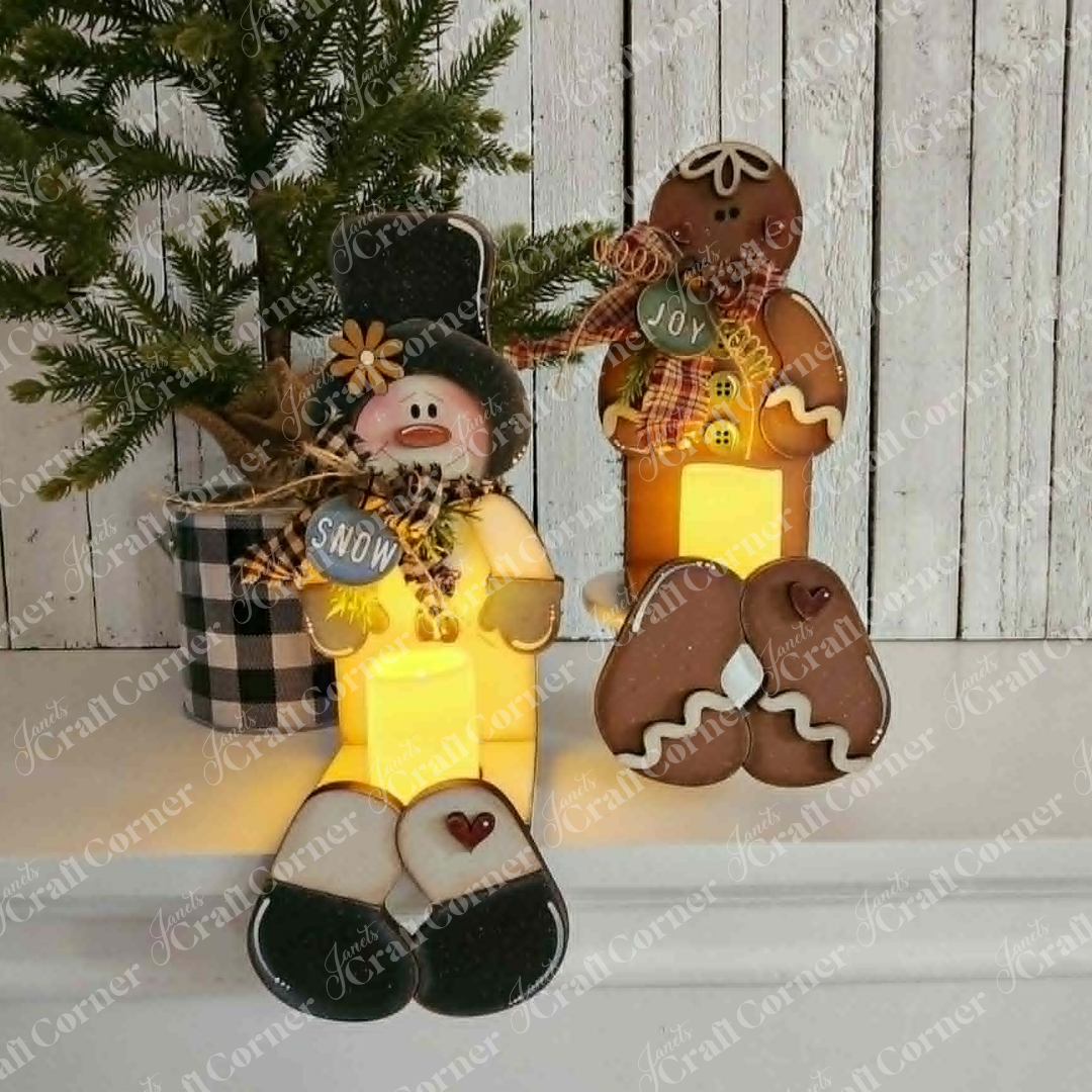 Brighten your holiday decor with Janet’s Craft Corner Snowman & Gingerbread Votive Holder Shelf Sitters DIY home decor craft kit. This set features two charming figurines—a snowman holding a “Snow” sign and a gingerbread person with a “Joy” sign—seated in front of a plaid pot topped with a pine tree, all against a rustic white wooden wall. Perfect for adding festive warmth and cheer to any space, these delightful shelf sitters make an inviting addition to your Christmas home decor.