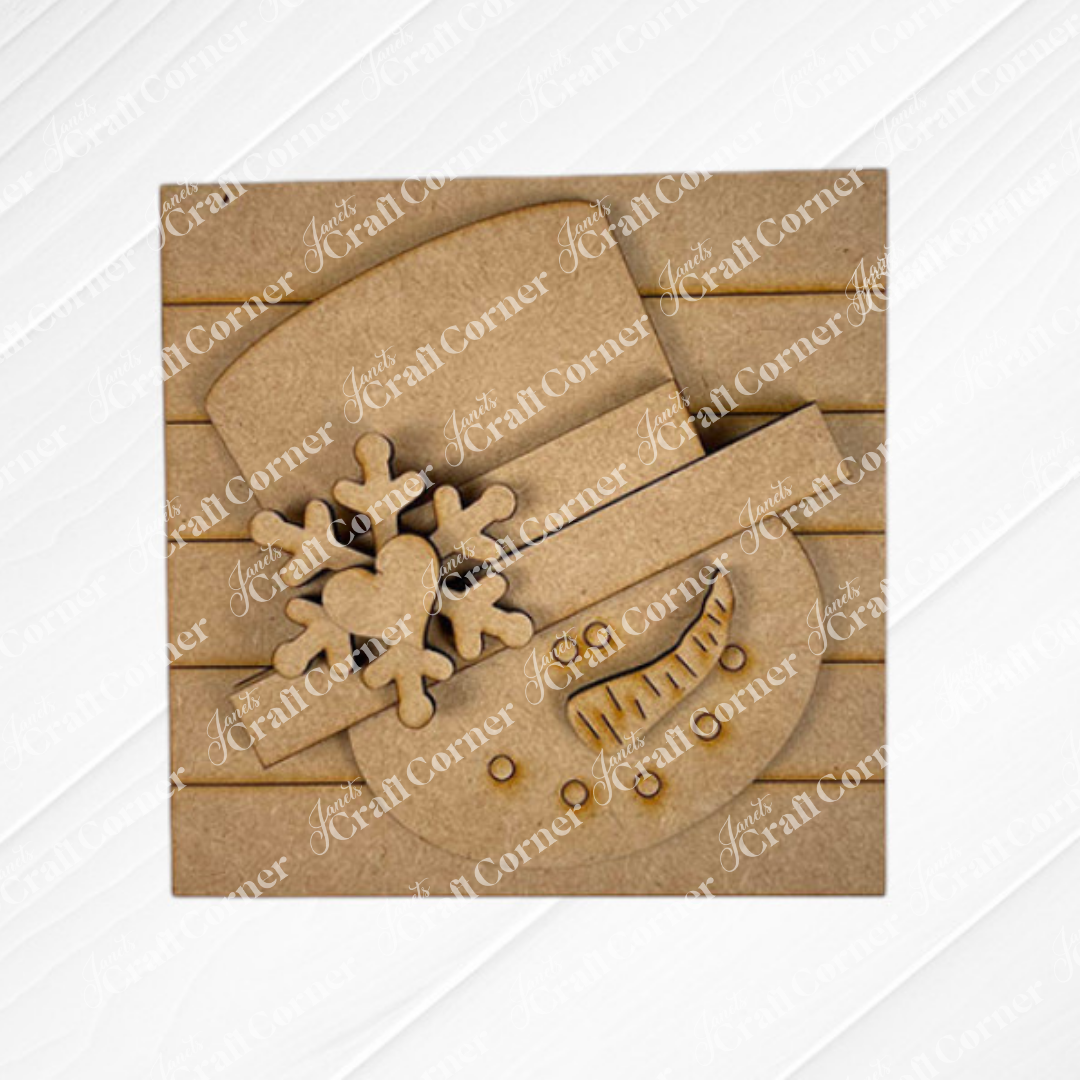 The Snow Squares from Janet's Craft Corner feature a snowman face cutout with a carrot nose, smile, heart-accented snowflake, and pair perfectly with swappable signs for festive DIY home decor.