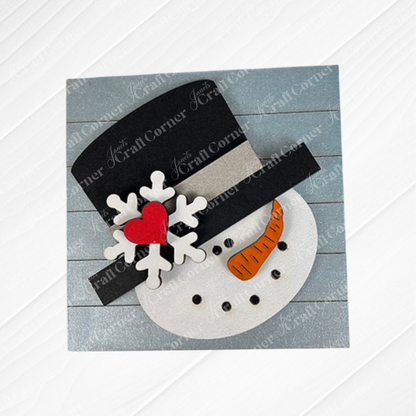 Snow Squares by Janet's Craft Corner features a charming snowman face with a black top hat, red heart, white snowflake, and orange carrot nose on a blue wooden background—perfect seasonal decor for Swappable Square Displays.