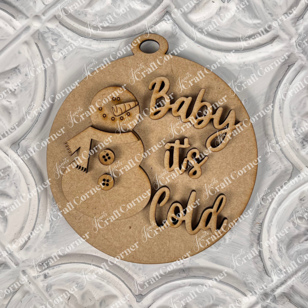 Introducing Janet's Craft Corner's Round Christmas Ornaments from their DIY Decoration Kits: A delightful ornament featuring a snowman cutout and the words "Baby it's Cold" on a beautifully textured background. This festive piece combines playful lettering and winter imagery, set amidst an array of decorative patterns.