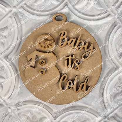 Introducing Janet's Craft Corner's Round Christmas Ornaments from their DIY Decoration Kits: A delightful ornament featuring a snowman cutout and the words "Baby it's Cold" on a beautifully textured background. This festive piece combines playful lettering and winter imagery, set amidst an array of decorative patterns.