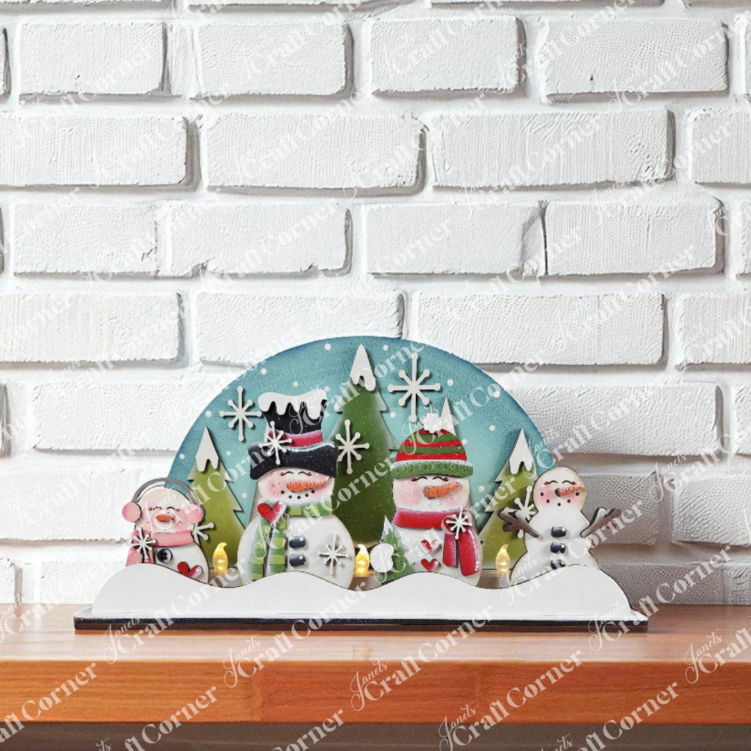 Janet's Craft Corner's Snowman Tealight Shelf Sitter features cheerful snowmen, a reindeer, and trees on a snowy blue sky—perfect for adding festive charm to any shelf.