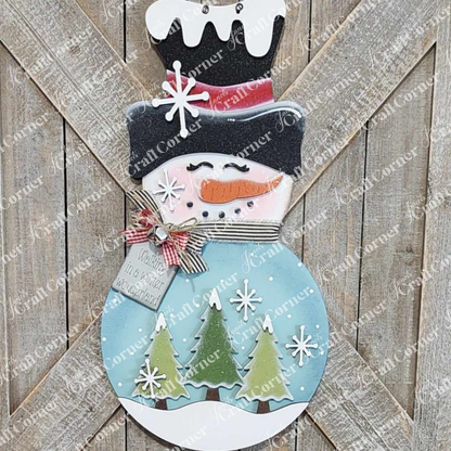 The Snowman Trees Wall/Door Hanger by Janet's Craft Corner is a DIY seasonal home decor craft kit featuring a snowman with hat, carrot nose, pink cheeks, and scarf amid green trees and snowflakes—a rustic festive touch for your space.