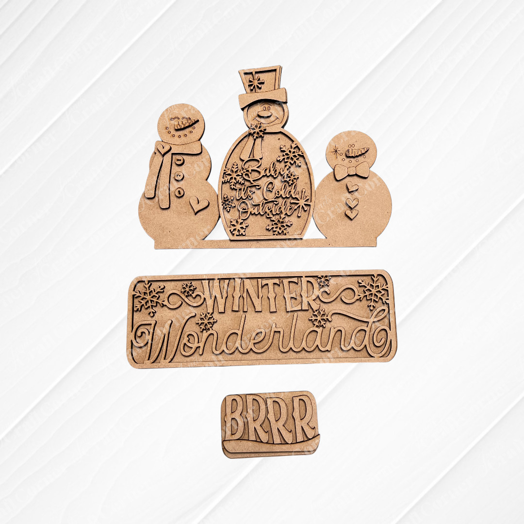 Wooden cutouts on a textured, white square background showcase two snowmen—one adorned with a top hat and scarf, the other smaller. The text "Winter Wonderland" and "BRRR" is displayed in decorative lettering. Ideal for personalized home décor, the burlap surface beneath adds a cozy touch. This is the Winter Wonderland Interchangeable Insert by Janet's Craft Corner.
