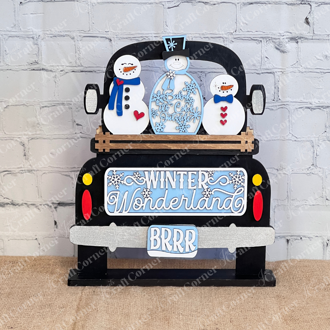 Janet's Craft Corner presents the "Winter Wonderland Interchangeable Insert - DIY Craft Kit - Set of 1," a decorative wooden sign featuring a truck with three snowmen dressed in winter attire. This home decor piece, perfect for creative enthusiasts, reads "Winter Wonderland" and "BRRR," and showcases snowflake accents against a brick wall and burlap surface.