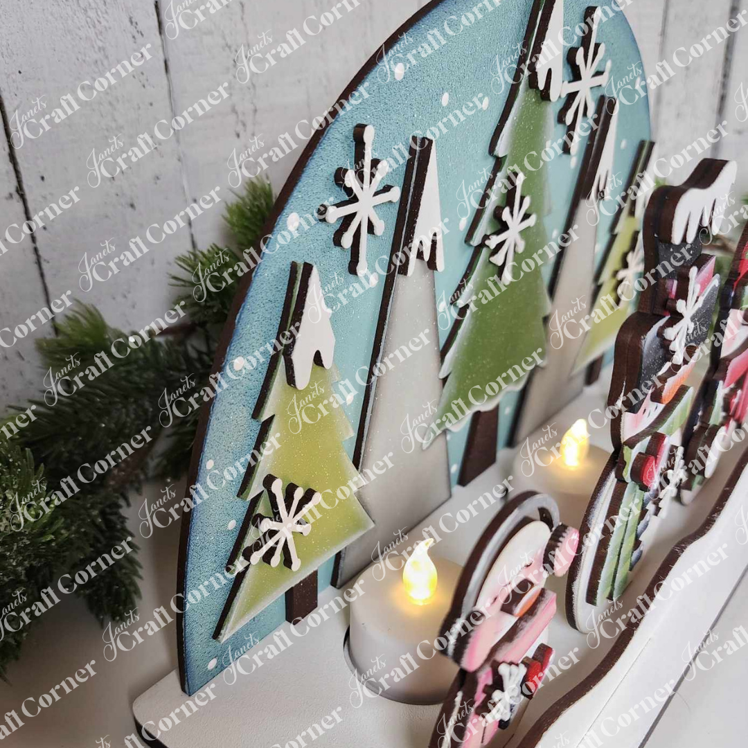 The Snowman Tealight Shelf Sitter by Janet's Craft Corner is a DIY kit featuring layered trees and snowflakes on blue, with small LED candles at the base—perfect for creating charming seasonal decor for your home.