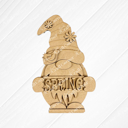 The Spring Sign Gnome Shelf Sitter by Janet's Craft Corner is a delightful DIY seasonal home decor kit. It includes a charming wooden gnome with a flower-detailed hat and bird, holding a "SPRING" sign against burlap with an embossed white pattern, perfect for enhancing your home.