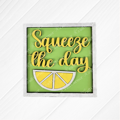 The Lemon Squares sign from Janet's Craft Corner features "Squeeze the day" in yellow script above a lemon slice, set on a green background and framed in white wood. This Swappable Squares DIY decor is perfect for seasonal home styling.