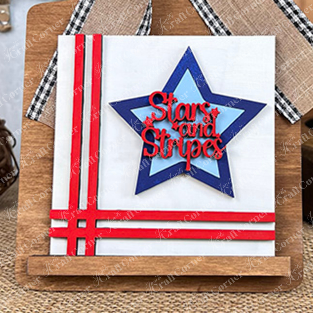 The Patriotic Squares DIY craft kit from Janet's Craft Corner features a square white sign with red stripes and a blue star, perfect for home decor or July 4th celebrations—display it on the included wooden stand.