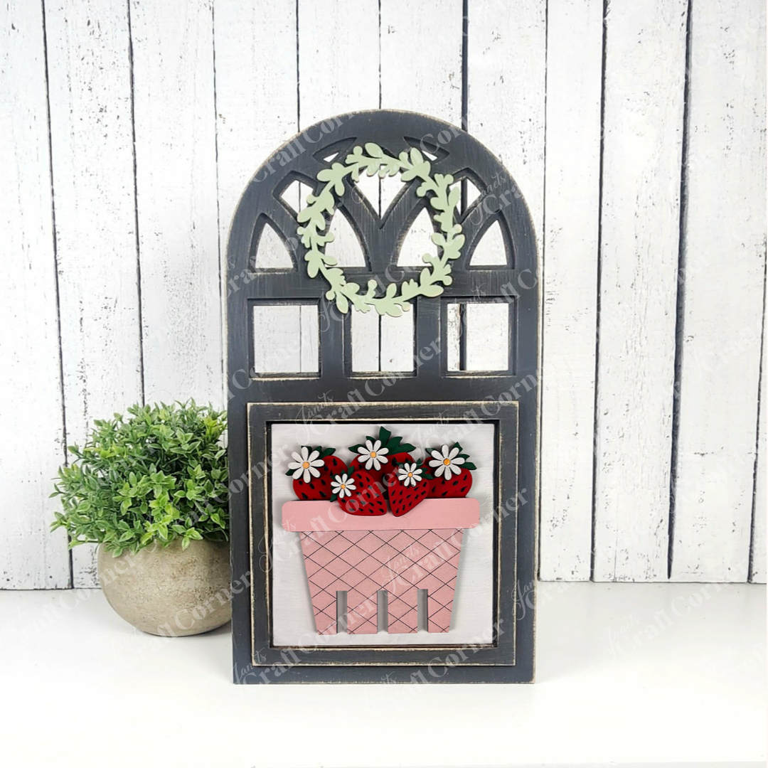 Janet's Craft Corner’s Strawberry Swappable Squares DIY kit creates a window-shaped wooden sign with a green wreath, pink flower box with red strawberries and white flowers, perfect for tiered tray decor beside a potted plant.