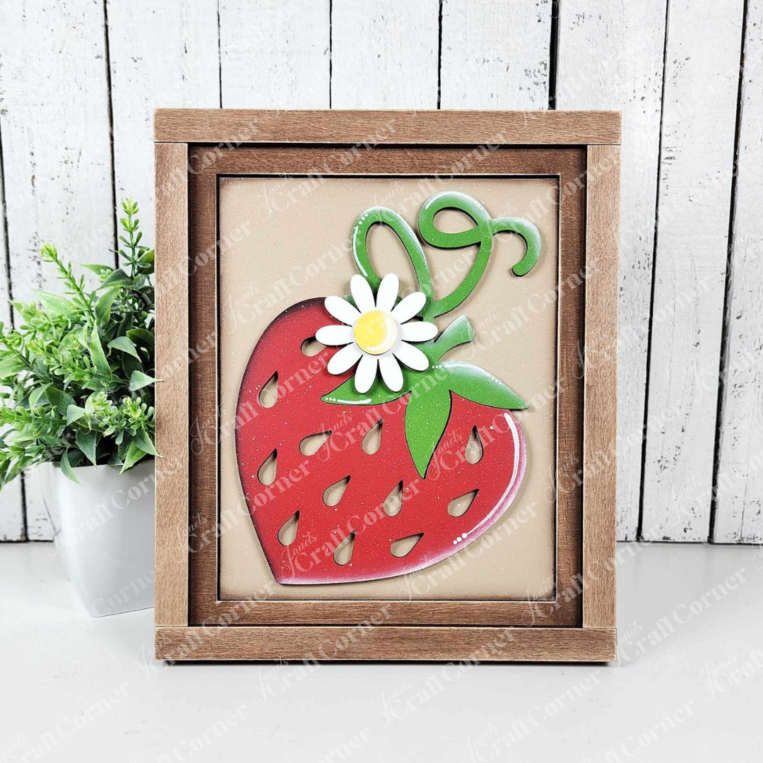 A painted sample of a sign from Janet's Craft Corner's Berry Sweet Switchable Farmhouse Signs DIY home decor craft kit is displayed against a white shiplap wall. The Strawberry Farmhouse Sign features a red strawberry, green leaves, and daisy on beige in a wooden frame—ideal for seasonal home decor. 