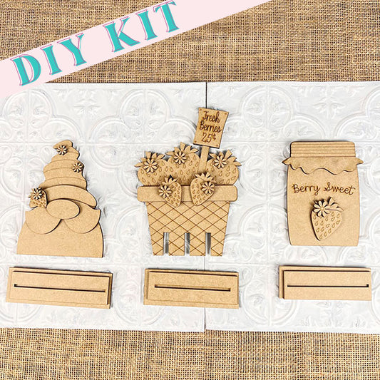 Introducing Janet's Craft Corner's latest product: the Strawberry Mini Shelf Sitters. This farmhouse chic DIY craft kit showcases strawberry-themed mini wood signs, complete with wooden cutouts of a layered cake, a flower basket adorned with a "Fresh Berries 25¢" sign, and a charming "Berry Sweet" jar. These elements are perfectly designed against a burlap and white textured background.