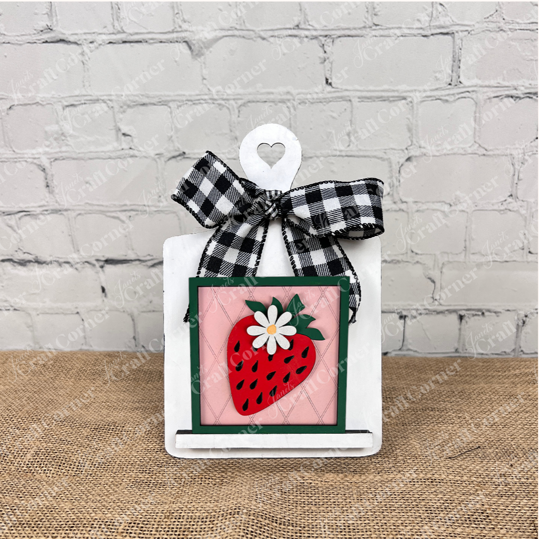 Janet's Craft Corner Strawberry Swappable Squares is a DIY seasonal home decor kit featuring a small white cutting board with heart cutout, plaid bow, and framed strawberry and daisy design—perfect for tiered trays.