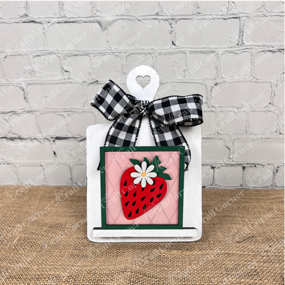 Janet's Craft Corner Strawberry Swappable Squares is a DIY seasonal home decor kit featuring a small white cutting board with heart cutout, plaid bow, and framed strawberry and daisy design—perfect for tiered trays.