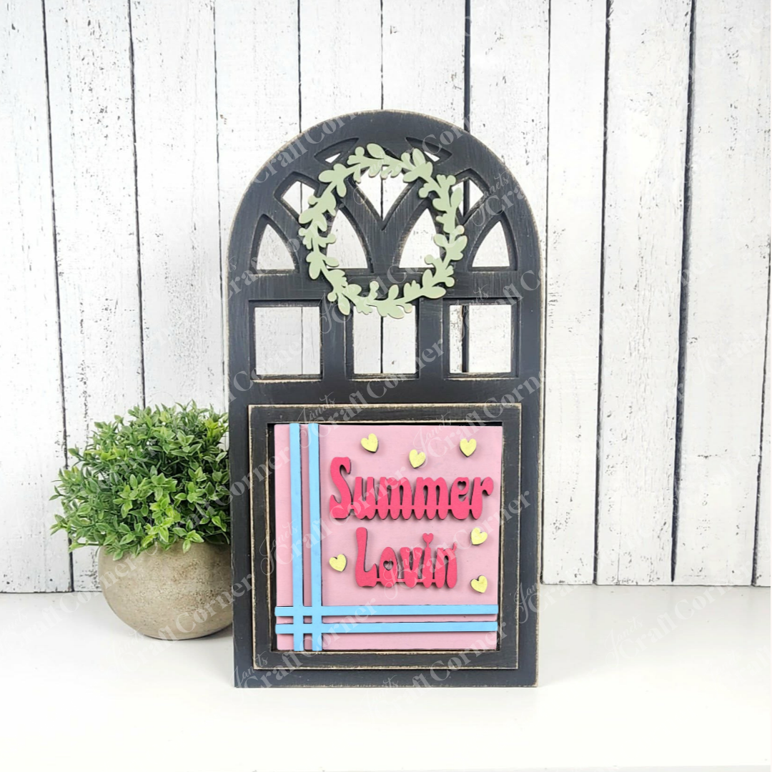 Janet's Craft Corner’s Summer Lovin Swappable Squares DIY kit features wood cut-outs, a green wreath, and pink “Summer Lovin’” plaque with blue stripes and yellow hearts—ideal tiered tray decor beside a potted plant.