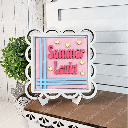 Janet's Craft Corner's Summer Lovin Swappable Squares DIY kit features a pink “Summer Lovin” sign with blue stripes and yellow hearts, displayed on a stand—ideal seasonal decor for your tiered tray or shelf.