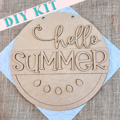 Introducing the Janet's Craft Corner "Hello Summer Watermelon Round," a round wooden sign blank adorned with "hello SUMMER" in decorative font and featuring cut-out watermelon seed details. It's perfect for home décor and rests on a burlap surface with a cheerful "DIY KIT" label, making it the ideal project to infuse your space with the Hello Summer Watermelon vibe.