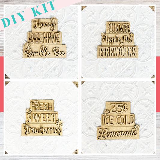 Image of Janet's Craft Corner's Summer Word Stacks DIY kit, which includes four farmhouse-style wooden signs with engraved text: "Honey BEEhive Bumble Bee," "SUMMER Apple Pie FIREWORKS," "FRESH SWEET Strawberries," and "25¢ ICE COLD Lemonade." Perfect for summer displays on a white embossed surface.