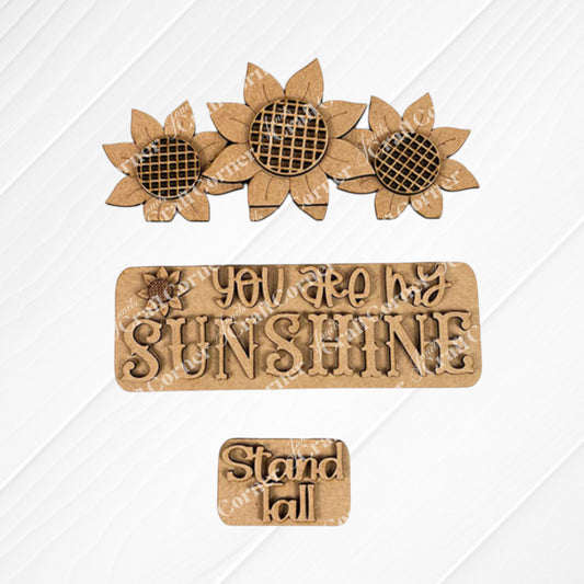 Sunflower accents on a textured backdrop: featuring three sunflowers at the top, a central plaque displaying "YOU ARE MY SUNSHINE," and a smaller plaque with "Stand Tall" positioned below. This delightful DIY kit from Janet's Craft Corner, known as the Sunflower Interchangeable Insert, is ideal for fans of versatile home decor themes.