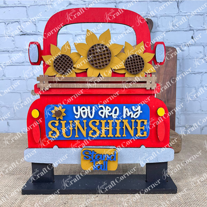 The Antique Truck Base with Interchangeable Insert from Janet's Craft Corner is a decorative piece shaped like the back of an antique truck adorned with sunflowers. It features the text "You are my sunshine" and "Stand tall," set against a white brick wall on a burlap surface. This DIY home decor kit is ideal for crafting hand-painted interchangeable inserts.