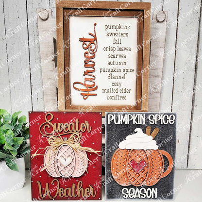 Three autumn-themed decorative signs on a wooden surface with a plant in the background.