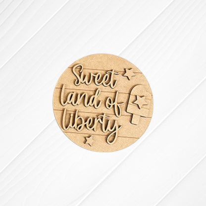 Janet's Craft Corner Patriotic Mini Shelf Sitters DIY Craft Kit features a round wooden sign with “Sweet land of liberty” in cursive, stars, and a popsicle—ideal for Americana décor or as festive accents on any shelf.