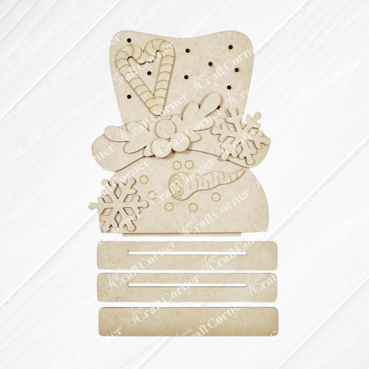 Add a delightful touch to your holiday décor with the Sweet Snowman Lighted Shelf Sitter from Janet’s Craft Corner. This beige snowman-shaped cutout features a top hat adorned with holly, a candy cane, and intricate snowflakes—making it a charming shelf sitter. Below, three rectangular sections rest on a light textured background, providing both style and space for creative decoration. Ideal as festive holiday home décor or as part of your next DIY craft project kit!.