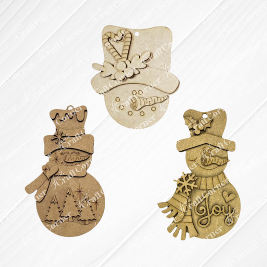 The Sweet Winter Snowmen Ornaments DIY holiday craft kit from Janet’s Craft Corner includes your choice of three wood and cardboard snowman ornaments, each adorned with winter-themed designs, hats, and scarves—an adorable set perfect for adding festive cheer to your Christmas tree ornament collection. Shown against a light background.