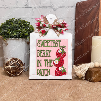 A charming sign with a bow, strawberries, and daisies saying "Sweetest Berry in the Patch" is shown on Janet's Craft Corner Breadboard Sign Holder for Switchable Farmhouse Signs, surrounded by rustic decor and plants.