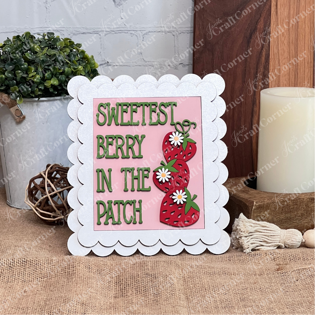 Janet's Craft Corner Single Scallop Trim Farmhouse Frame features a pink background with three strawberries and "Sweetest Berry In The Patch" in green, scalloped white edges—ideal for rustic tabletops or DIY craft displays.