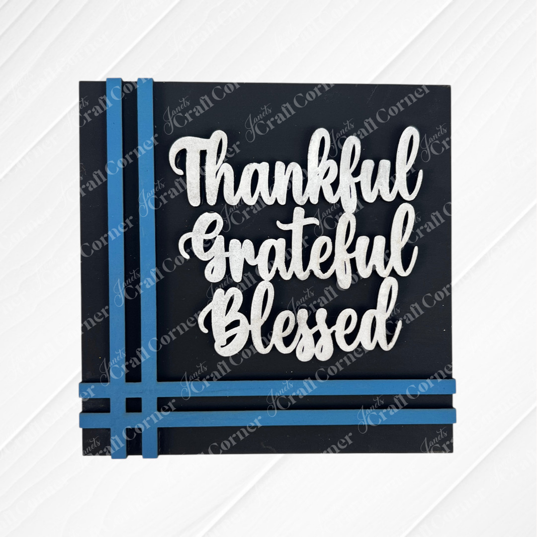 The Harvest Blessings Thanksgiving Squares from Janet's Craft Corner feature "Thankful Grateful Blessed" in bold white script on a black sign with blue ribbon accents, ideal as tiered tray decor or displayed with other Swappable Squares.