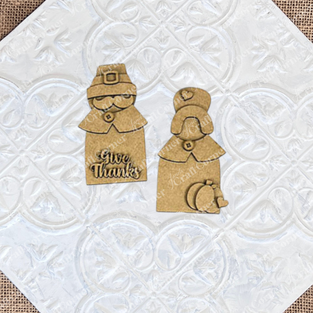 Introducing the "Give Thanks/Thanksgiving Tiered Tray Kit" from Janet's Craft Corner: this charming set includes wooden cutouts of a pilgrim couple with "Give Thanks" inscribed on one, complete with small stand bases. Ideal for home décor or as an accent piece for a tiered tray, these figures are stylized with hats and collars and come accompanied by an apple and pumpkin cutout.