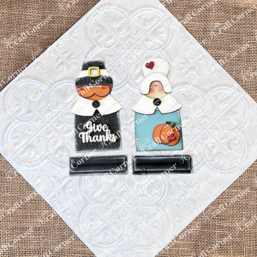 Introducing the "Give Thanks/Thanksgiving Tiered Tray Kit" from Janet's Craft Corner: this charming set includes wooden cutouts of a pilgrim couple with "Give Thanks" inscribed on one, complete with small stand bases. Ideal for home décor or as an accent piece for a tiered tray, these figures are stylized with hats and collars and come accompanied by an apple and pumpkin cutout.