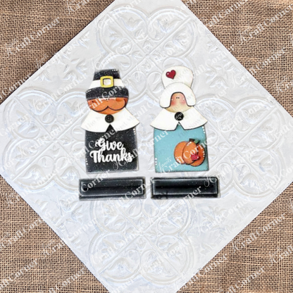 Introducing the "Give Thanks/Thanksgiving Tiered Tray Kit" from Janet's Craft Corner: this charming set includes wooden cutouts of a pilgrim couple with "Give Thanks" inscribed on one, complete with small stand bases. Ideal for home décor or as an accent piece for a tiered tray, these figures are stylized with hats and collars and come accompanied by an apple and pumpkin cutout.