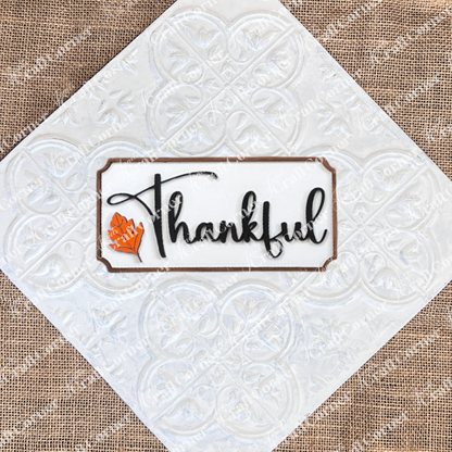 The Thankful Mini Shelf Sitter from Janet's Craft Corner is a DIY seasonal home decor kit featuring "Thankful" in black cursive and an orange leaf on a white wood background—ideal for personalized autumn decorations.