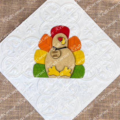 The Give Thanks/Thanksgiving Tiered Tray Kit by Janet's Craft Corner includes a DIY wooden turkey craft kit with a "gobble gobble" tag. It's perfect for enhancing your home décor and adding charm to your tiered tray setup against a simple backdrop.