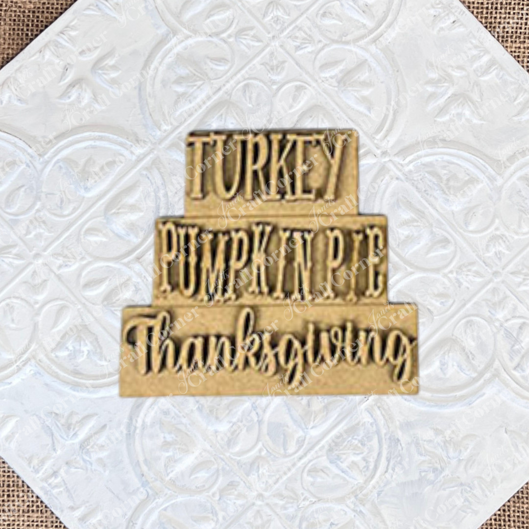 The Give Thanks/Thanksgiving Tiered Tray Kit by Janet's Craft Corner includes a stacked wooden sign featuring the words "Turkey," "Pumpkin Pie," and "Thanksgiving" arranged in three tiers, ideal for decorating your tiered tray. The kit also contains two separate wooden pieces to add delightful accents to your home décor.
