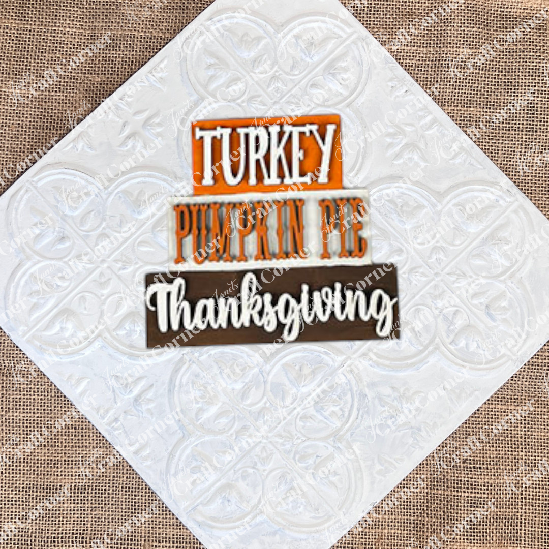 The Give Thanks/Thanksgiving Tiered Tray Kit by Janet's Craft Corner includes a stacked wooden sign featuring the words "Turkey," "Pumpkin Pie," and "Thanksgiving" arranged in three tiers, ideal for decorating your tiered tray. The kit also contains two separate wooden pieces to add delightful accents to your home décor.