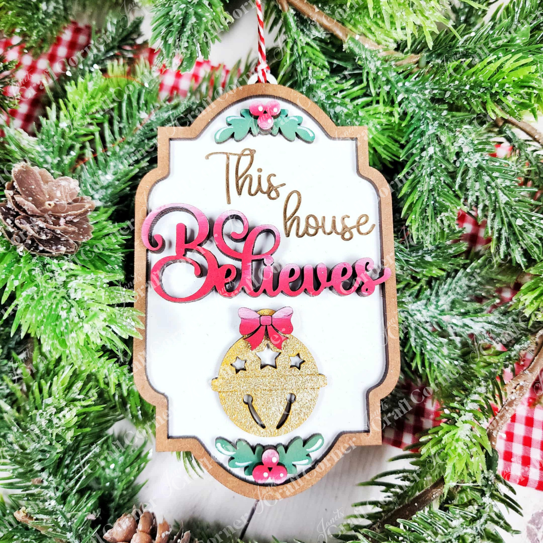 Add festive flair to your home with Janet's Craft Corner North Pole Ornaments—this DIY seasonal decor kit includes 1 ornament reading “This house Believes” in gold and red, adorned with a jingle bell, bow, and red flowers.