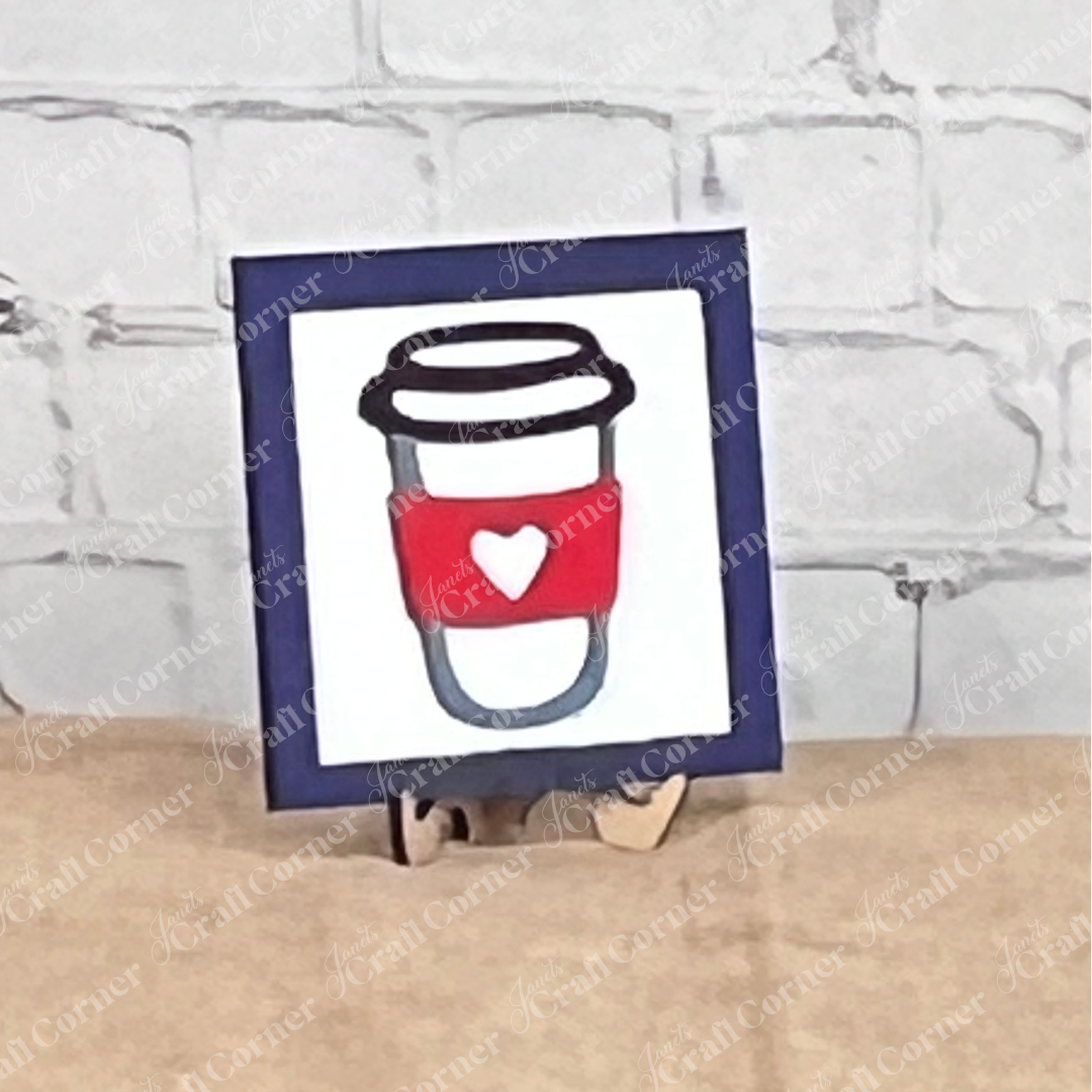 Coffee Bar Swappable Squares by Janet's Craft Corner: a framed drawing of a coffee cup with a red sleeve and white heart, displayed on wood risers as charming DIY home decor against a white brick wall.