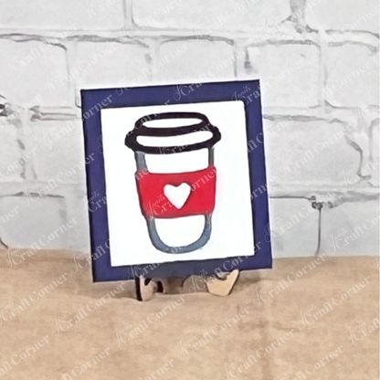 Coffee Bar Swappable Squares by Janet's Craft Corner: a framed drawing of a coffee cup with a red sleeve and white heart, displayed on wood risers as charming DIY home decor against a white brick wall.
