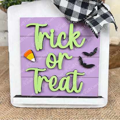 Janet's Craft Corner's Halloween Squares sign features "Trick or Treat" in green on purple, with candy corn, black bats, a checkered bow, and wood cut-outs—perfect tiered tray décor for Halloween.
