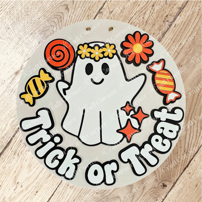 The Groovy Ghost Trick or Treat Wall Hanger by Janet's Craft Corner is a DIY craft kit featuring a smiling ghost with a yellow flower crown, candies, and “Trick or Treat” text—perfect for decorating any wooden surface this Halloween.