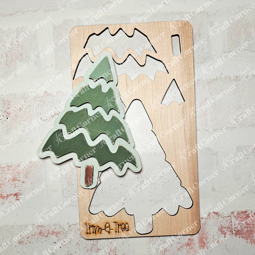 The Trim a Tree Kids Pop-Out Kit from Janet's Craft Corner features a green tree with wavy branches as part of its wooden puzzle. This DIY craft kit includes individual pieces that resemble various parts of the tree, all set on a white puzzle board where each piece fits snugly into its cutout.