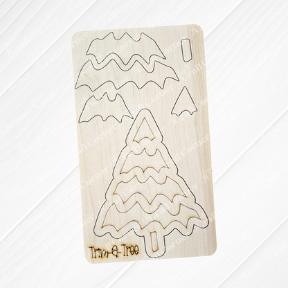 Experience the finest in holiday decor with Janet's Craft Corner's "Trim a Tree Kids Pop-Out Kit." This DIY craft kit features a wooden Christmas tree project. The stylized tree showcases wavy branch patterns and an engraved "Trim-a-Tree" on its base. Set against a white wood wall, it serves as a charming accent for any festive setting.