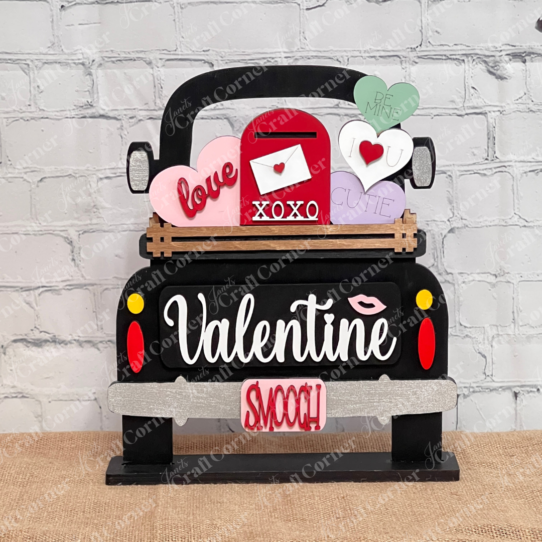 Janet's Craft Corner's DIY kit features an Antique Truck Base with heart cutouts that say "love," "xoxo," "cutie," and "be mine." This interchangeable home decor adds a rustic charm to a white brick wall.