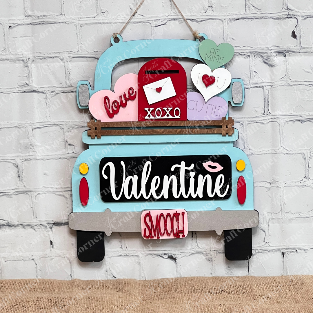 Janet's Craft Corner offers the Valentine Interchangeable Insert DIY home decor kit, a decorative wooden sign shaped like a vintage truck with hearts and an envelope, featuring words like "love," "XOXO," and "cutie." Ideal for Valentine's Day, it hangs beautifully on a white brick wall.