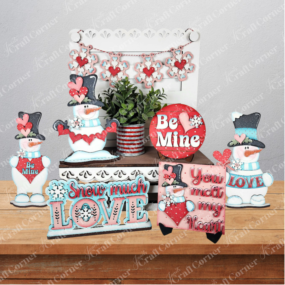 Janet’s Craft Corner Valentine Snowmen Decor Set is a DIY kit with wood cut-outs of snowmen, hearts, potted plants, and signs like “Be Mine” and “You melt my heart” in red, pink, blue, and white—perfect for charming Valentine’s Day decor.